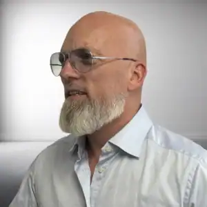 Billed af en voksen mand med skaldet hoved, skæg, briller og hvid skjorte.